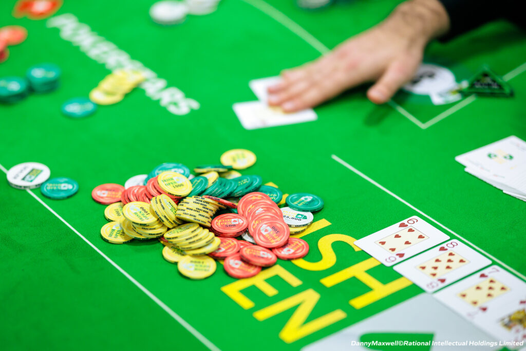 Ein professioneller Pokertisch mit grünem Filz, umgeben von Spielkarten, Pokerchips und Getränken. Vier Personen sitzen um den Tisch herum und konzentrieren sich auf ihre Karten
