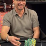 Ein professioneller Pokertisch mit grünem Filz, umgeben von Spielkarten, Pokerchips und Getränken. Vier Personen sitzen an dem Tisch und spielen Poker.