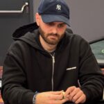 Ein professioneller Pokertisch mit grünem Filz, umgeben von Spielkarten, Pokerchips und Getränken. Mehrere Personen sitzen um den Tisch herum und spielen Poker.