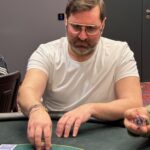 Ein professioneller Pokertisch mit grünem Filz, umgeben von Spielkarten, Pokerchips und Getränken. Zwei Spieler sitzen gegenüber und konzentrieren sich auf ihre Karten.