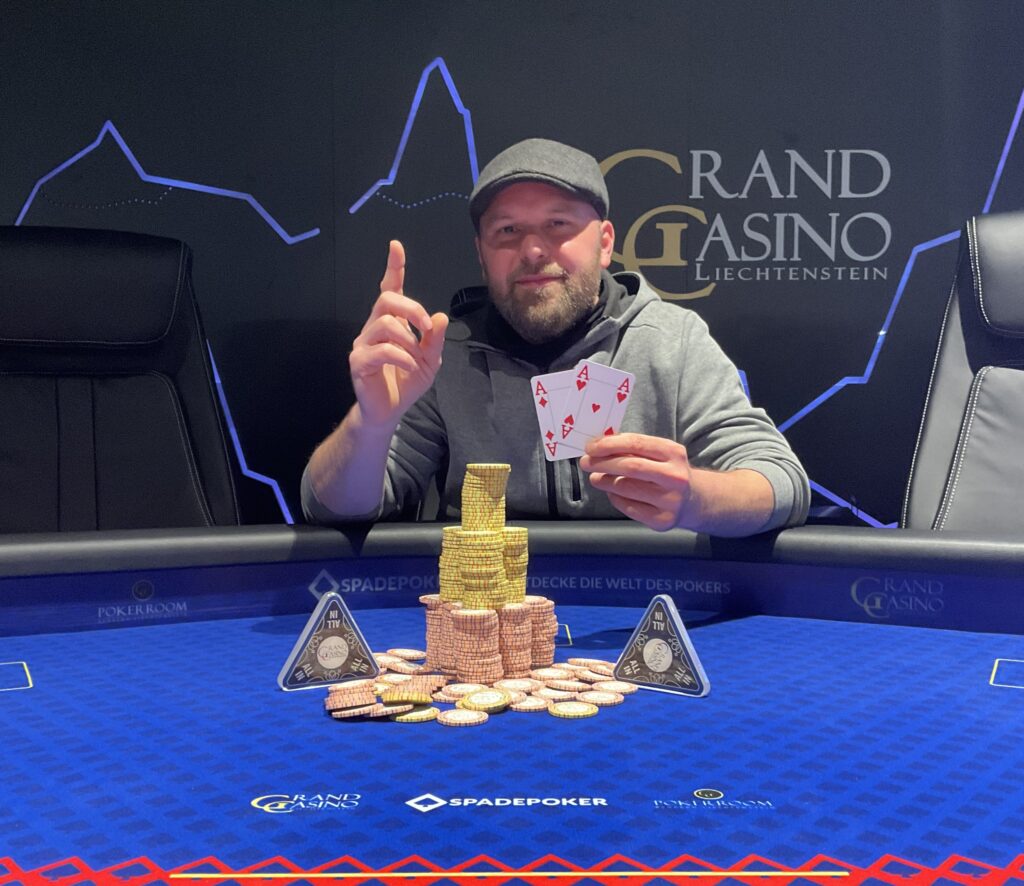 Ein Mann und eine Frau sitzen an einem Pokertisch und halten Karten in der Hand, während sie konzentriert auf ihre Gegner schauen. Im Hintergrund sind Pokerchips und Getränke zu sehen.