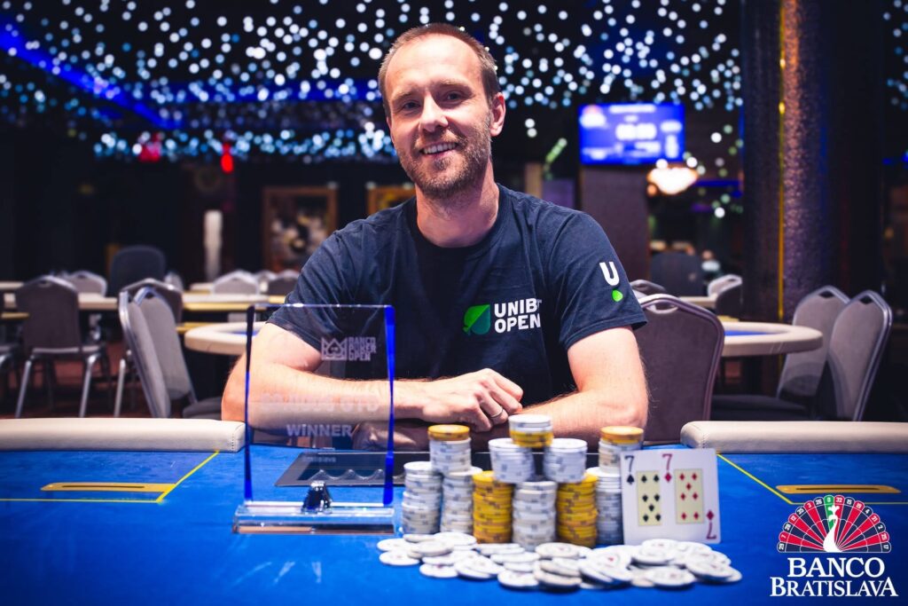 Ein professioneller Pokertisch mit grünem Filz, umgeben von Stühlen und Pokerchips. Zwei Spieler sind erkennbar und halten Karten in der Hand, während sie konzentriert auf ihre Hände sch