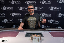 Ein Mann mit einem breiten Lächeln und einer Sonnenbrille sitzt an einem Pokertisch, umgeben von Chips und Spielkarten. Er hält triumphierend eine Gewinntrophäe in die Luft.