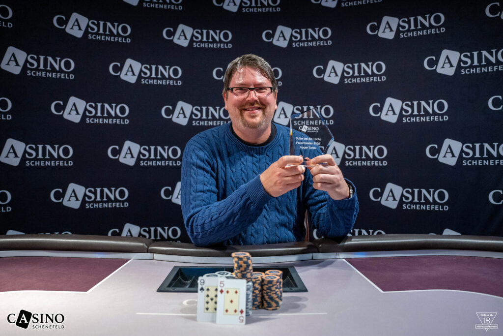 Ein glücklicher Pokerspieler feiert seinen Sieg bei einem Hyper-Turbo-Turnier. Er hält freudig seine Karten in die Luft, umgeben von Konfetti und jubelnden Zuschau