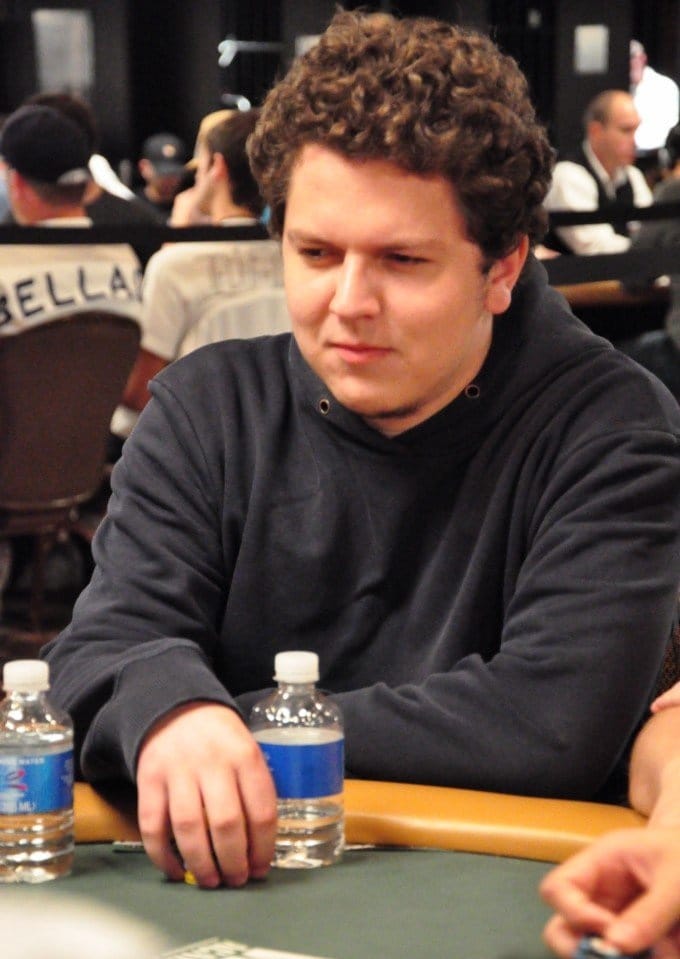 Ein Spieler mit Sonnenbrille und Kappe sitzt an einem Pokertisch während der World Series of Poker 2009. Im Hintergrund sind weitere Spieler und Zuschauer zu sehen.