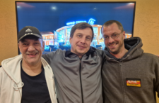 Ein Team von Pokerspielern posiert vor einem Banner des World College of Advanced Poker. Jeder trägt ein offizielles WCOAP-Trikot und lächelt in die Kamera.