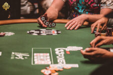 Ein Mann sitzt an einem Pokertisch während eines Turniers der World Series of Poker (WSOP). Er hat eine Sonnenbrille auf und betrachtet konzentriert seine Karten. Im Hintergrund sind andere Spieler und