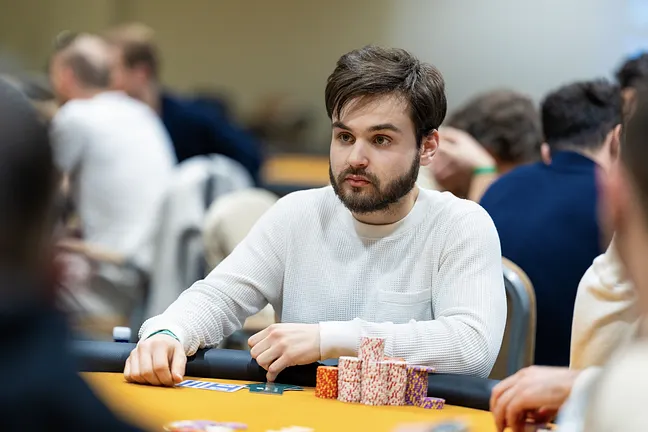 Ein professioneller Pokerspieler mit Sonnenbrille und Kappe, der seine Karten auf einem grünen Pokertisch betrachtet.