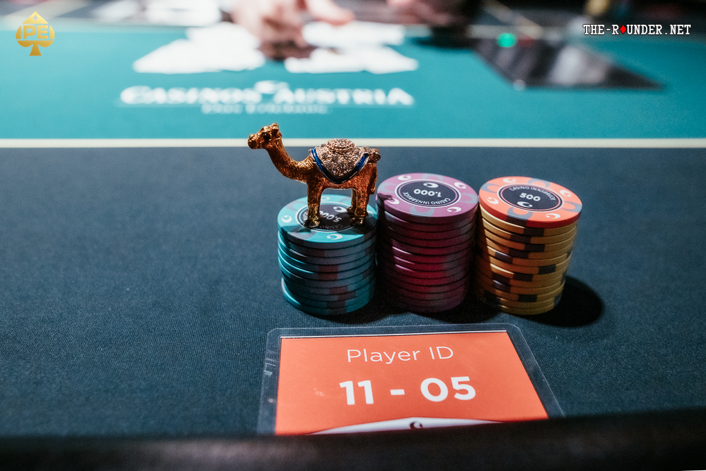 Ein Mann und eine Frau spielen Poker an einem Tisch in einem eleganten Casino. Der Mann hat Karten in der Hand und setzt Chips, während die Frau konzentriert ihre Karten betrachtet. Um sie herum stehen andere
