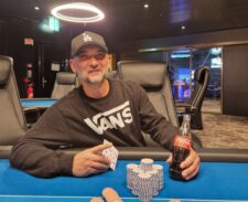 Ein Mann spielt Poker am Tisch mit anderen Spielern in einem Casino. Er hat eine Hand mit Pokerchips vor sich und betrachtet seine Karten konzentriert.