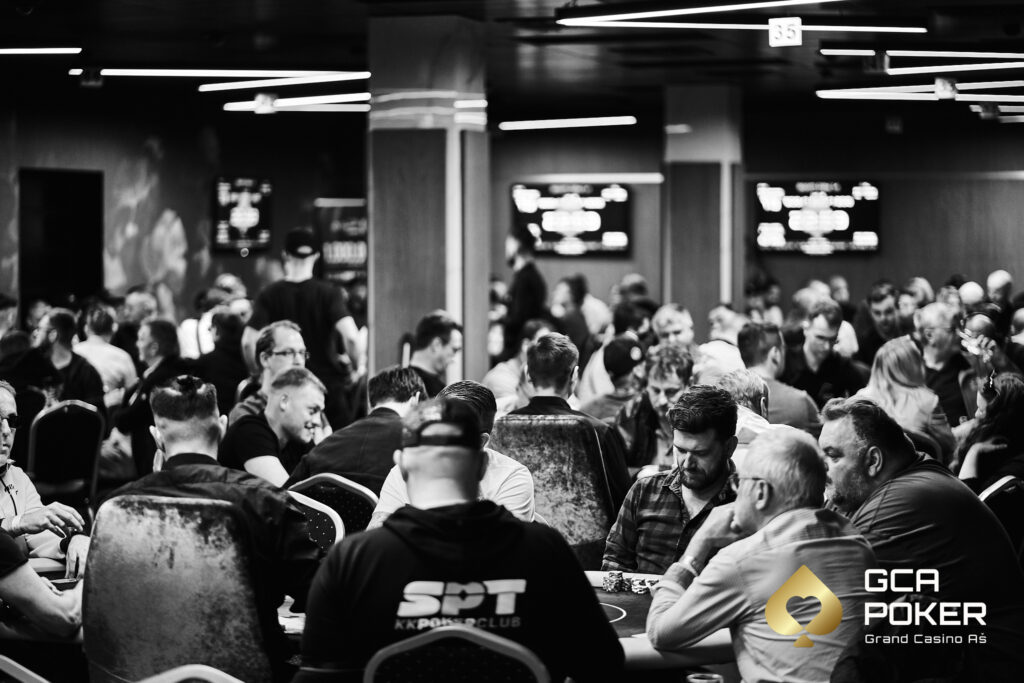 Ein Mann und eine Frau sitzen an einem Pokertisch im Casino. Der Mann mischt die Karten, während die Frau ihre Karten ansieht und konzentriert wirkt. Die Szene ist in einem eleganten Raum mit