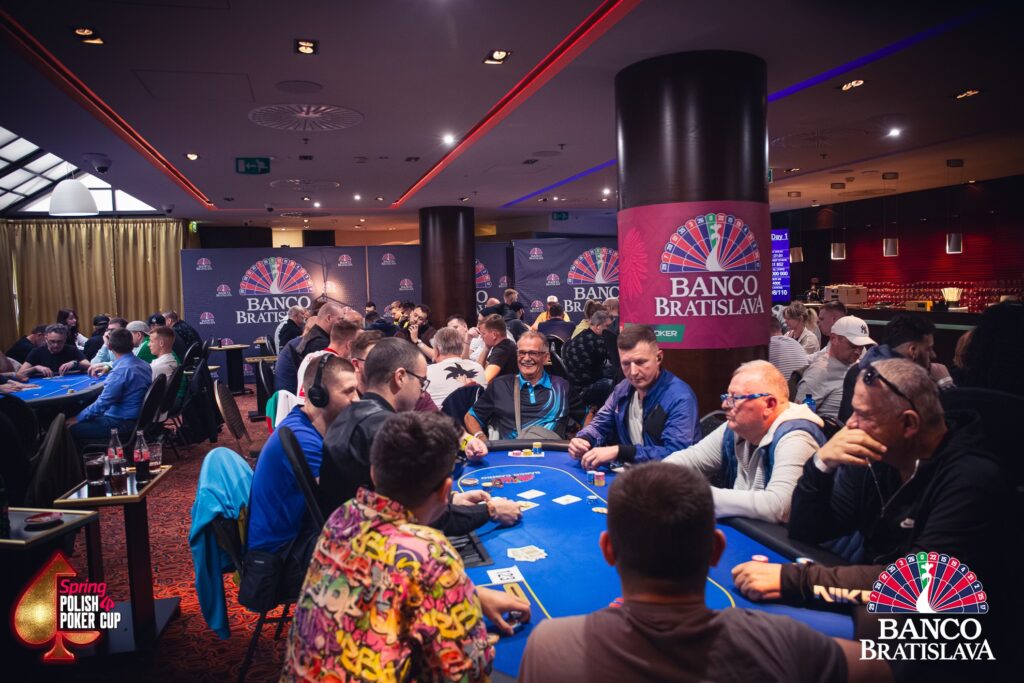 Ein Mann und eine Frau sitzen an einem Pokertisch und spielen Poker. Der Mann hat einen Stapel Chips vor sich, während die Frau Karten hält und konzentriert auf ihre Hand schaut.