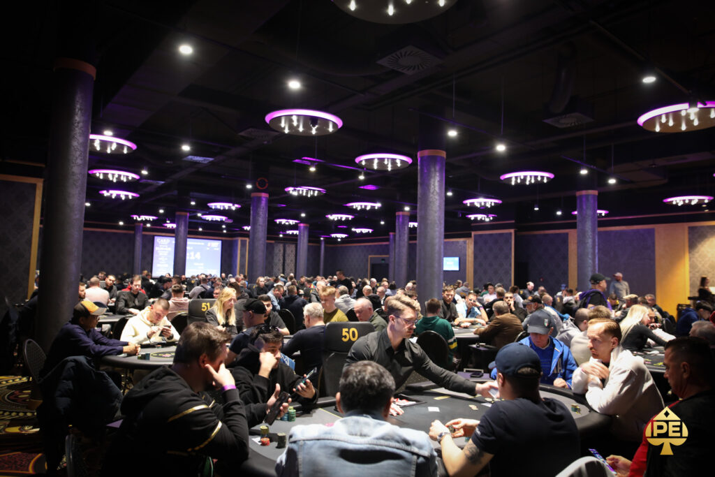 Ein Mann spielt Poker an einem Tisch mit grünem Filz und hält seine Karten in der Hand. Er hat eine ernste Miene und konzentriert sich auf das Spiel. Im Hintergrund sind Pokerchips