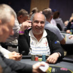 Ein Mann sitzt an einem Pokertisch, umgeben von Spielkarten und Chips. Er hält zwei Karten in der Hand und schaut konzentriert auf den Tisch.