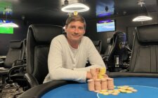 Ein Mann und eine Frau stehen auf einer Klippe und betrachten den Sonnenuntergang über dem Ozean. Sie halten sich an den Händen und lächeln.