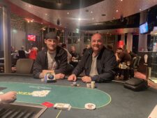Ein Mann spielt Poker an einem Tisch in einem eleganten Casino. Er hat einen ernsten Gesichtsausdruck und hält seine Karten in der Hand. Im Hintergrund sind andere Spieler und Dealer zu sehen.