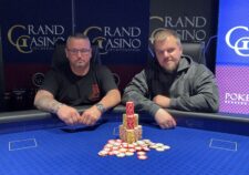 Ein Mann und eine Frau sitzen an einem Pokertisch und spielen eine Partie Poker. Der Mann hält Karten in der Hand und schaut konzentriert auf den Tisch, während die Frau ihm gegenüber mit ernstem Ges
