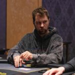 Ein Mann und eine Frau sitzen an einem Pokertisch und spielen ein Spiel. Der Mann hält Karten in der Hand, während die Frau konzentriert auf ihre Karten schaut. Im Hintergrund sind Pokerchips und