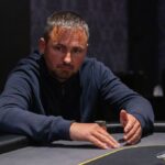 Ein Mann und eine Frau sitzen an einem Pokertisch, halten Karten in der Hand und betrachten konzentriert ihre Gegner. Eine grüne Filzdecke bedeckt den Tisch, im Hintergrund sind