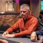 Ein Mann spielt Poker an einem Tisch in einem Casino, umgeben von anderen Spielern und Chips.
