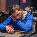 Ein Mann und eine Frau sitzen an einem Pokertisch, halten Karten in den Händen und schauen konzentriert auf den Tisch. Im Hintergrund sind Pokerchips und Getränke zu sehen.