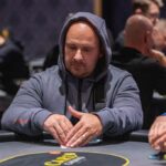 Ein Poker-Tisch mit grüner Spielfläche, umgeben von Spielkarten, Pokerchips und Getränken. Menschen sitzen um den Tisch herum, konzentriert auf ihre Karten und takt