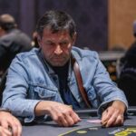 Ein Tisch mit grünem Filz, auf dem Pokerchips und Spielkarten liegen, umgeben von vier Personen, die Poker spielen.