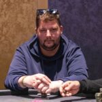 Ein glücklicher Mann und eine Frau sitzen an einem Pokertisch und lächeln, während sie Karten spielen. Der Mann hält ein Paar Asse in der Hand, während die Frau ihre Karten betrachtet. Im