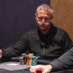 Ein Mann und eine Frau spielen Poker in einem eleganten Casino. Der Mann hat Karten in der Hand und schaut konzentriert auf den Tisch, während die Frau mit gespanntem Blick ihre Chips arrangiert. Die Atmosph