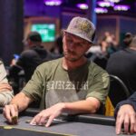 Ein Mann und eine Frau sitzen an einem Pokertisch und spielen Poker. Der Mann hält Karten in der Hand, während die Frau mit ernstem Gesichtsausdruck auf ihre Karten schaut. Das Bild zeigt eine span