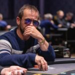 Ein Mann und eine Frau sitzen an einem Pokertisch und spielen Karten. Der Mann hat eine Hand mit Assen, während die Frau ernsthaft ihre Karten betrachtet. Im Hintergrund sind Pokerchips und Getr