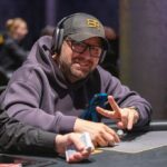 Ein Mann und eine Frau sitzen an einem Pokertisch und spielen Texas Hold'em. Der Mann hat eine Hand mit Karten in der Hand und schaut konzentriert auf den Tisch, während die Frau mit einem Pokerchip spielt