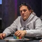 Ein Mann und eine Frau sitzen an einem Pokertisch und schauen konzentriert auf ihre Karten. Der Mann hat eine Kappe auf und die Frau trägt eine auffällige Halskette. Karten und Poker
