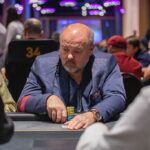 Ein Mann sitzt an einem Pokertisch und hält Karten in der Hand, während er konzentriert auf seine Gegner schaut.