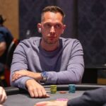 Ein Mann und eine Frau sitzen an einem Pokertisch, während sie konzentriert ihre Karten betrachten. Die Frau hält Chips in der Hand, während der Mann mit einem ernsten Gesichtsausdruck seine Hand über