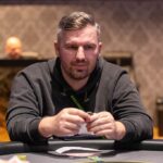 Ein Mann und eine Frau sitzen an einem Pokertisch und halten ihre Spielkarten in der Hand. Sie haben intensive Gesichtsausdrücke, während sie konzentriert auf das Spiel schauen. Im Hintergrund sind