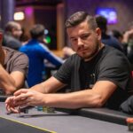 Ein Mann und eine Frau sitzen entspannt an einem Pokertisch und spielen Karten. Der Mann hält eine Hand mit Spielkarten, während die Frau ihre Karten betrachtet. Die Szene spielt sich in einem elegant