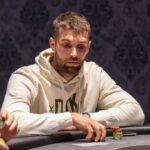 Ein glamouröses Casino-Interieur mit eleganten Kronleuchtern, roten Teppichen und Pokertischen, an denen Spieler in Anzügen und Krawatten sitzen.