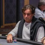 Ein Mann und eine Frau spielen Poker an einem eleganten Spieltisch in einem luxuriösen Casino. Der Mann hat eine Hand mit Karten, während die Frau konzentriert ihre Karten betrachtet. Im Hintergrund sind
