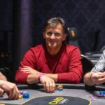 Ein Mann und eine Frau spielen Poker an einem eleganten Holztisch in einem stilvollen Wohnzimmer. Der Mann hat eine Hand mit Pokerchips und Karten, während die Frau konzentriert ihre Karten betrachtet. Im