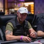 Ein Mann und eine Frau sitzen an einem Pokertisch und spielen Poker. Der Mann hat eine Hand mit Karten in der Luft und die Frau schaut konzentriert auf ihre Karten. Es herrscht eine spannende Atmos