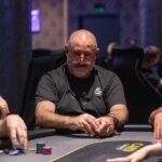 Ein Mann und eine Frau sitzen an einem Pokertisch und spielen eine Partie Poker. Der Mann hält Karten in der Hand und schaut konzentriert auf den Tisch, während die Frau ihre Karten betrachtet.