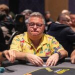 Ein Mann und eine Frau sitzen an einem Pokertisch und spielen Karten. Der Mann hält seine Karten geheim, während die Frau mit ernstem Gesichtsausdruck auf ihre Karten schaut. Im Hintergrund