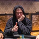 Ein Mann spielt Poker an einem eleganten Tisch in einem Casino, umgeben von anderen Spielern.