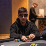 Ein professioneller Pokertisch mit grünem Filz, umgeben von Spielern, die Karten halten und Pokerchips stapeln.