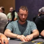 Ein Mann und eine Frau sitzen an einem Pokertisch und spielen Karten. Der Mann hält seine Karten in der Hand, während die Frau mit ernstem Gesichtsausdruck auf ihre Karten schaut. Im Hinter