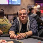 Ein Bild von einem Pokertisch mit Spielkarten, Pokerchips und Getränken, auf dem Spieler ihre Hände halten. Eine Atmosphäre von Spannung und Konzentration ist zu spüren.