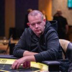 Ein professioneller Pokertisch mit grünem Filz und Spielkarten, umgeben von Pokerchips und Getränken, während Spieler konzentriert ihre Karten betrachten.