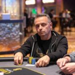 Ein professioneller Pokertisch mit Chips, Karten und Getränken, umgeben von Spielern in einem spannenden Turnier.