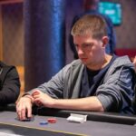 Ein Bild von vier Personen, die an einem Pokertisch sitzen und Karten spielen. Die Personen sind konzentriert und haben Pokerchips vor sich liegen.